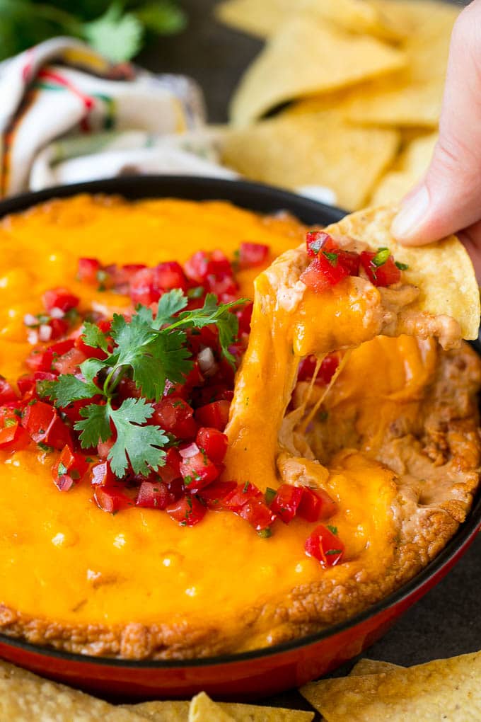 Bean Dip Recipe | Mexican Dip #dip #appetizer #mexicanfood #beans #cheese #ezlod A tortilla chip scooping out a serving of Mexican bean dip.