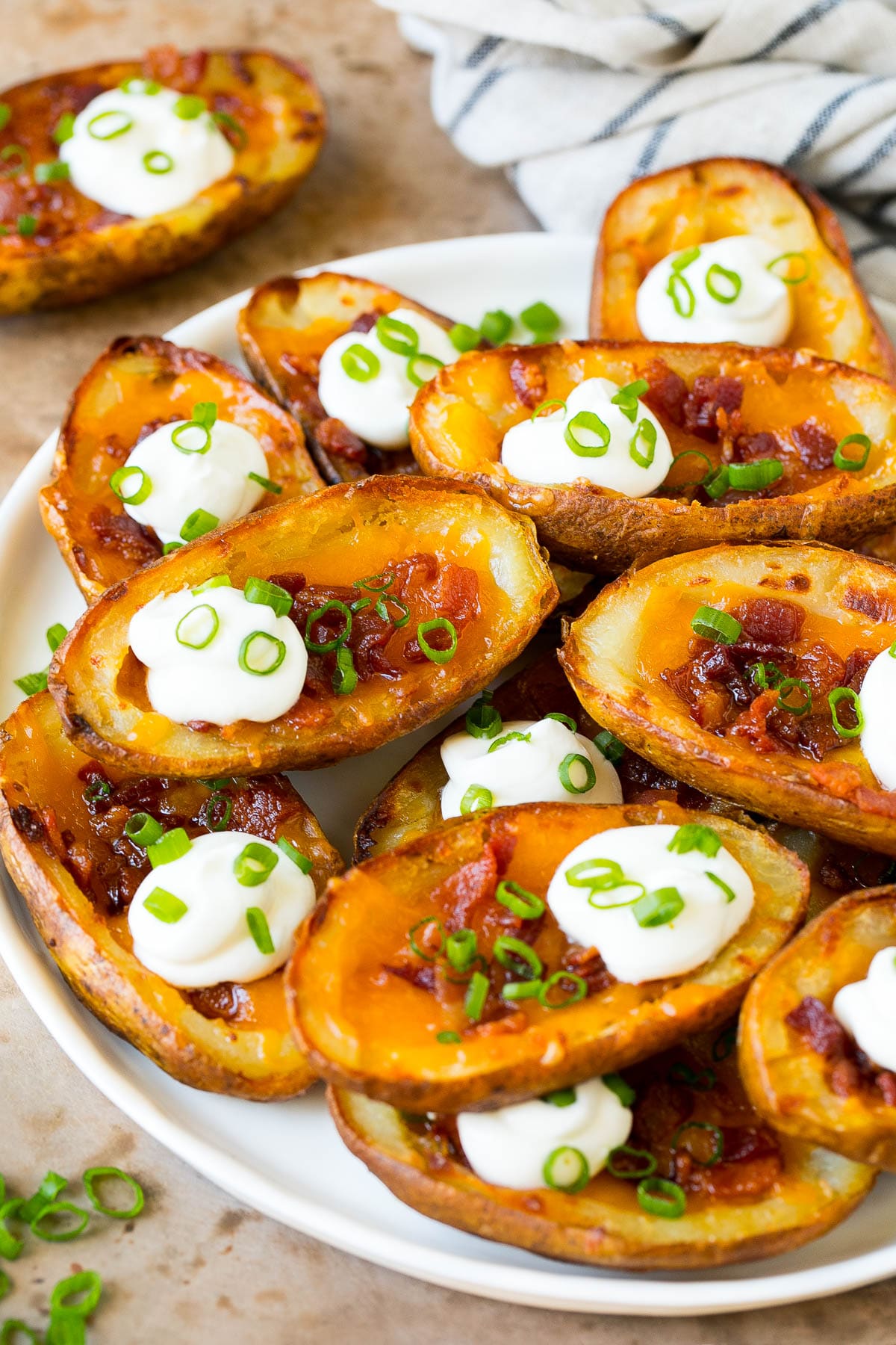 Potato Skins Recipe | Loaded Potatoes #potatoes #appetizer #snack #cheese #bacon #ezlod A serving plate of potato skins topped with bacon and sour cream.