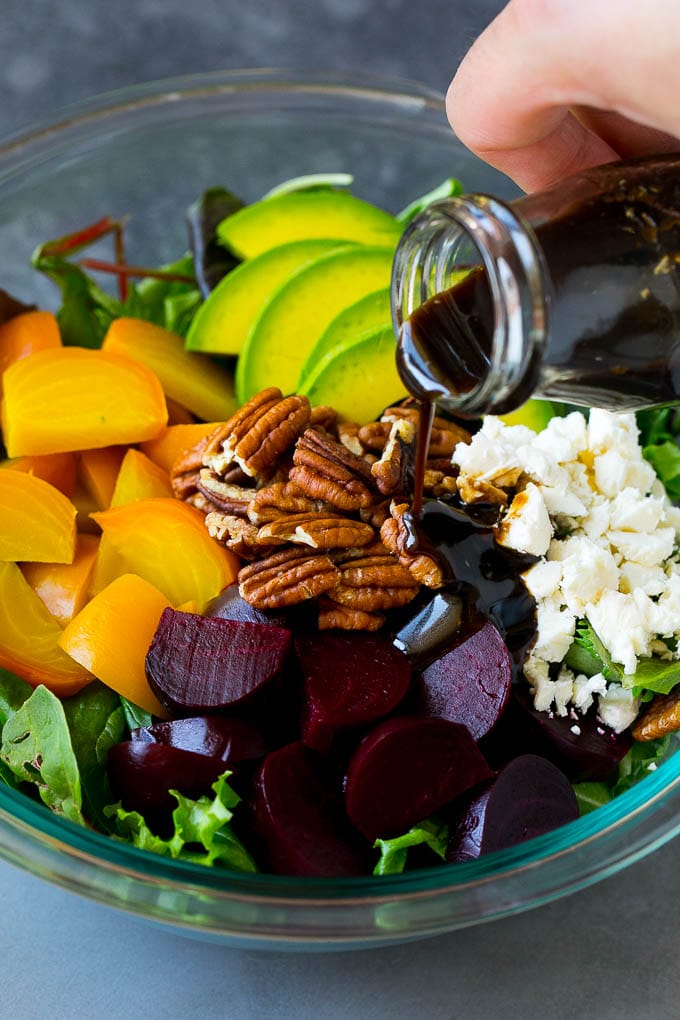 Beet Salad Recipe #beets #avocado #feta #salad #dinner #ezlod Balsamic dressing being poured over beets, sliced avocado and feta cheese.