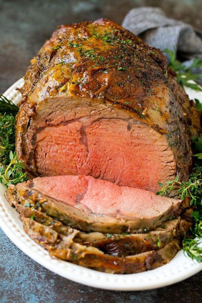Prime Rib Recipe #primerib #beef #roast #dinner #thanksgiving #christmas #keto #lowcarb #ezlod A sliced slow roasted prime rib roast surrounded by fresh herbs.