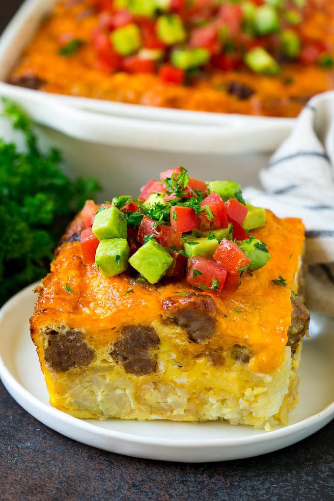 Sausage Egg Casserole Recipe | Egg Casserole #eggs #sausage #potato #cheese #casserole #breakfast #brunch #ezlod A slice of sausage egg casserole with a garnish of fresh tomatoes.