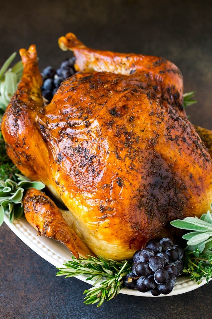 Thanksgiving Turkey Recipe | Roasted Turkey #turkey #thanksgiving #fall #dinner #ezlod A whole roasted Thanksgiving turkey on a platter that's decorated with grapes and herbs.