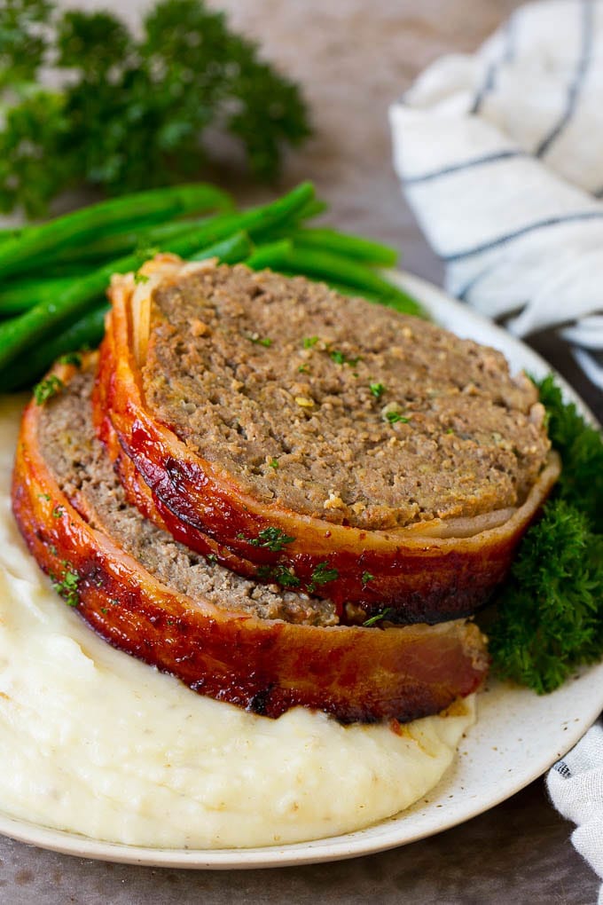 Bacon Wrapped Meatloaf Recipe | Beef Meatloaf #meatloaf #beef #groundbeef #bacon #dinner #ezlod Slices of bacon wrapped meatloaf served over mashed potatoes with green beans.
