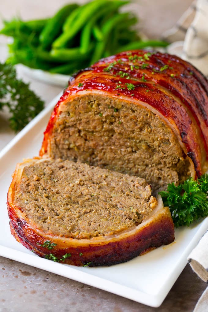 Bacon Wrapped Meatloaf Recipe | Beef Meatloaf #meatloaf #beef #groundbeef #bacon #dinner #ezlod A bacon wrapped meatloaf with a slice out of it, on a serving platter.