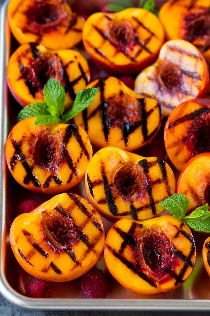 These grilled peaches are seared on the grill until tender and caramelized, then brushed with cinnamon honey for a sweet finish. Grilled peaches garnished with raspberries and fresh mint.