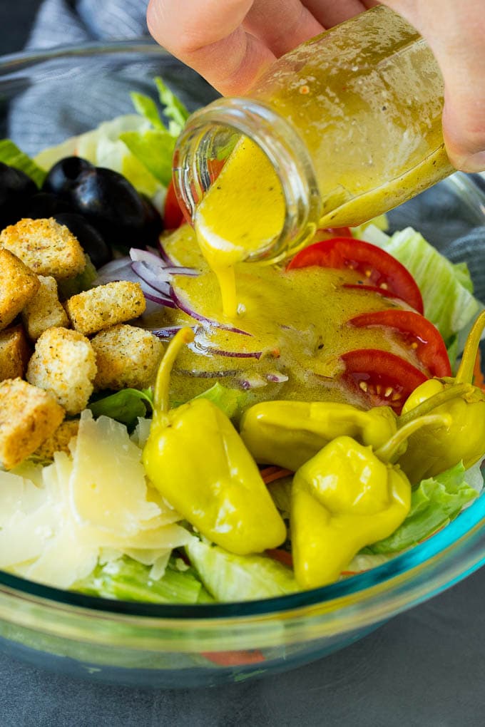 Olive Garden Salad Recipe | Italian Salad #salad #lettuce #olives #sidedish #dinner #ezlod Dressing being poured over a bowl of salad.