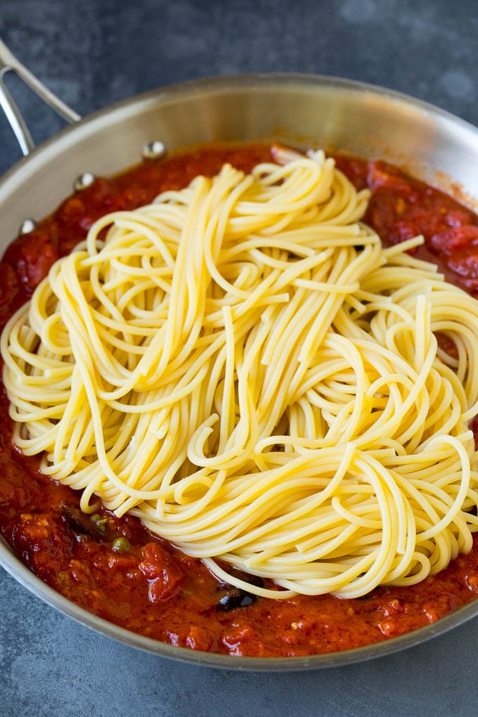 Pasta Puttanesca Recipe #pasta #tomatoes #olives #italianfood #dinner #ezlod Spaghetti in a pan of tomato sauce with olives and capers.