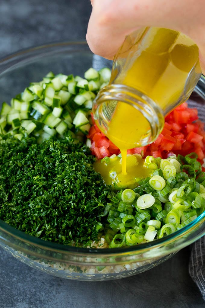 Tabbouleh Salad | Tabouli #salad #wheat #tomatoes #cucumber #healthy #sidedish #dinner #ezlod Dressing being poured into a bowl of bulgur wheat salad.