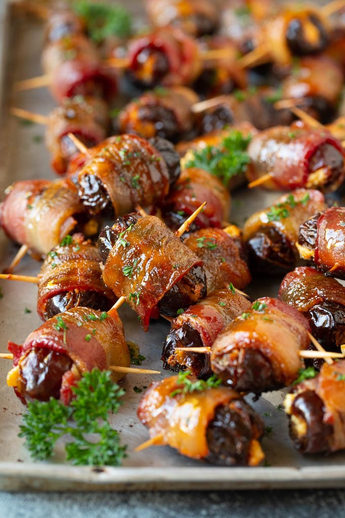 Bacon Wrapped Dates #appetizer #bacon #dates #cheese #ezlod Bacon wrapped dates on a sheet pan garnished with parsley.