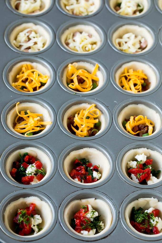 Mini Quiche Recipe #eggs #breakfast #brunch #appetizer #ezlod Muffin tins filled with pie crust, vegetables, meat and shredded cheese.