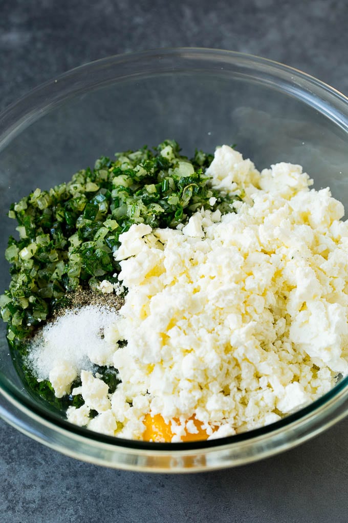 Spanakopita Recipe #appetizer #snack #spinach #cheese #ezlod Spinach, onions, herbs and feta cheese in a bowl.