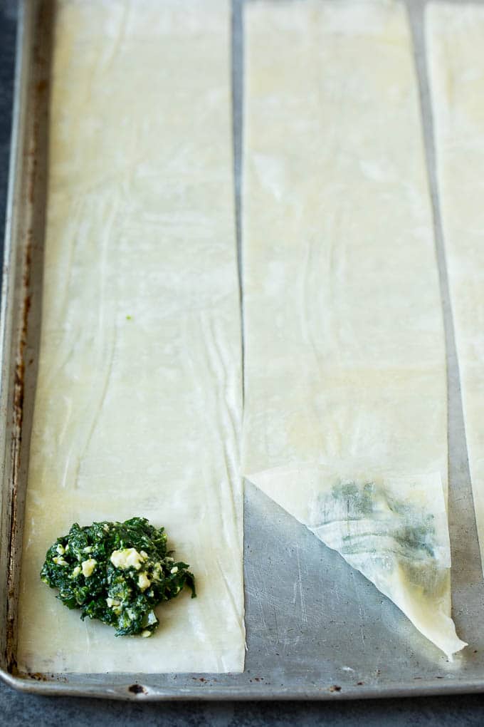 Spanakopita Recipe #appetizer #snack #spinach #cheese #ezlod Strips of phyllo dough with spoonfuls of filling on top.