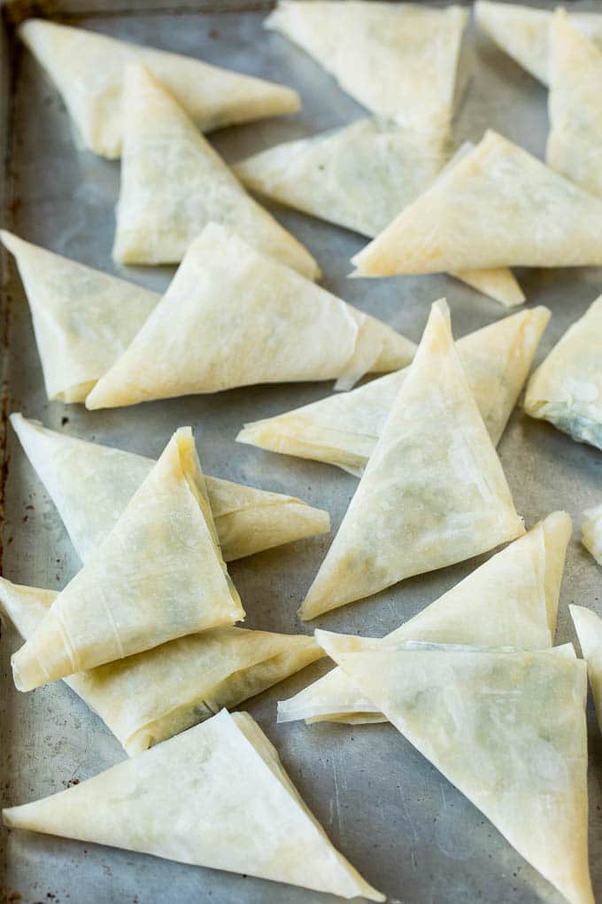 Spanakopita Recipe #appetizer #snack #spinach #cheese #ezlod Folded stuffed phyllo triangles on a sheet pan.