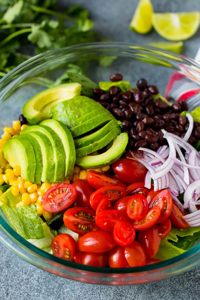 Mexican Salad Recipe #salad #corn #beans #avocado #tomatoes #ezlod Lettuce, tomatoes, onion, corn, avocado and black beans in a bowl.