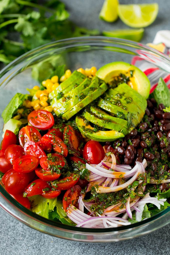 Mexican Salad Recipe #salad #corn #beans #avocado #tomatoes #ezlod Dressing poured over a bowl of lettuce, tomatoes, avocado and beans.
