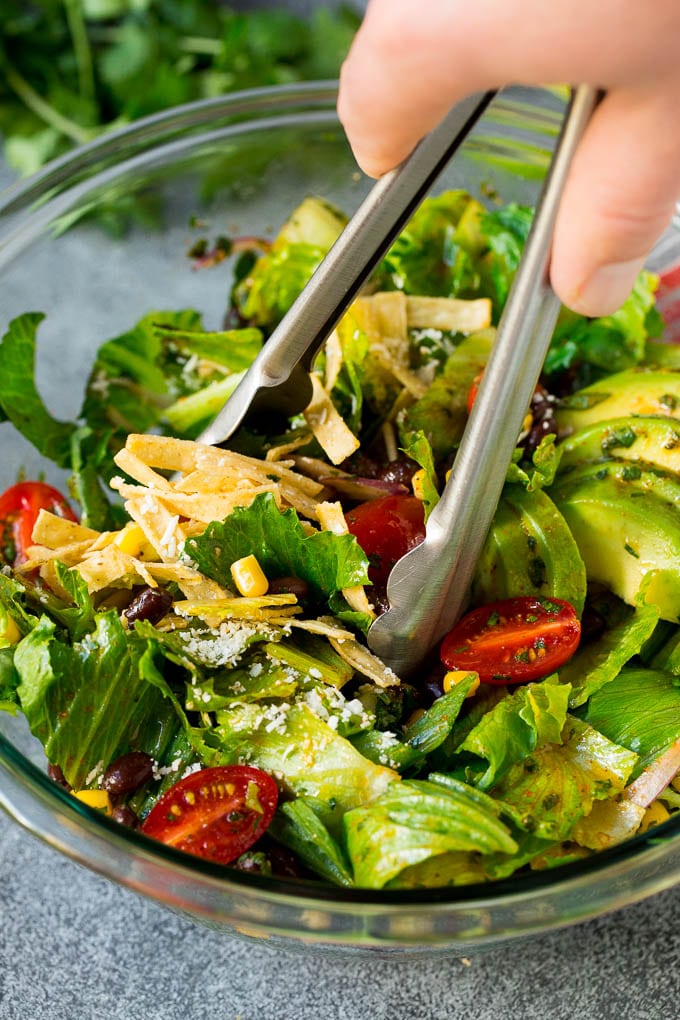 Mexican Salad Recipe #salad #corn #beans #avocado #tomatoes #ezlod Tongs serving up a portion of Mexican salad.