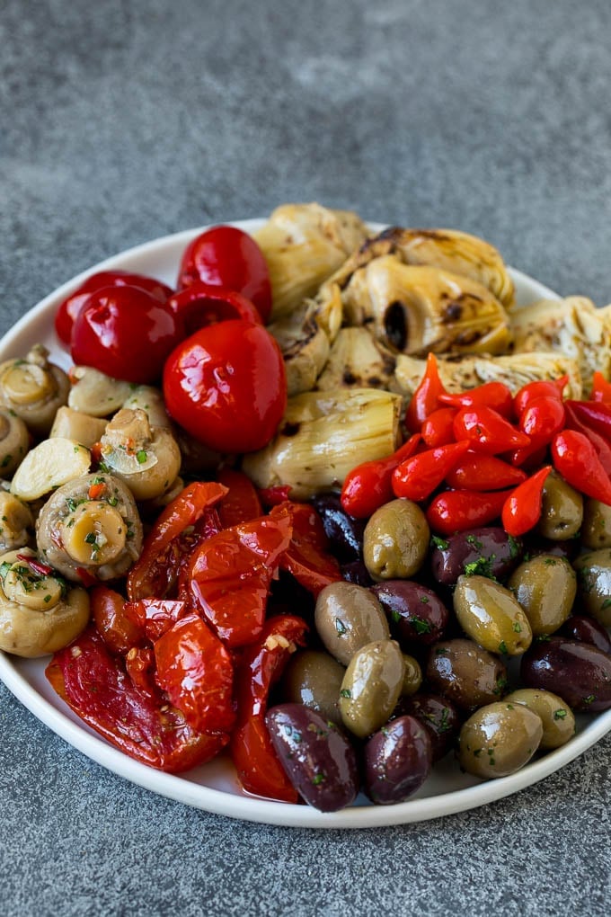 This mezze platter is filled with Mediterranean delicacies including dolmas, hummus, vegetables, pita bread and salads. #appetizer #ezlod A plate of olives, peppers and grilled artichokes.