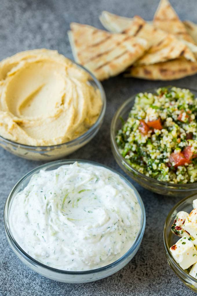 This mezze platter is filled with Mediterranean delicacies including dolmas, hummus, vegetables, pita bread and salads. #appetizer #ezlod Bowls of hummus, tzatziki and tabbouleh.