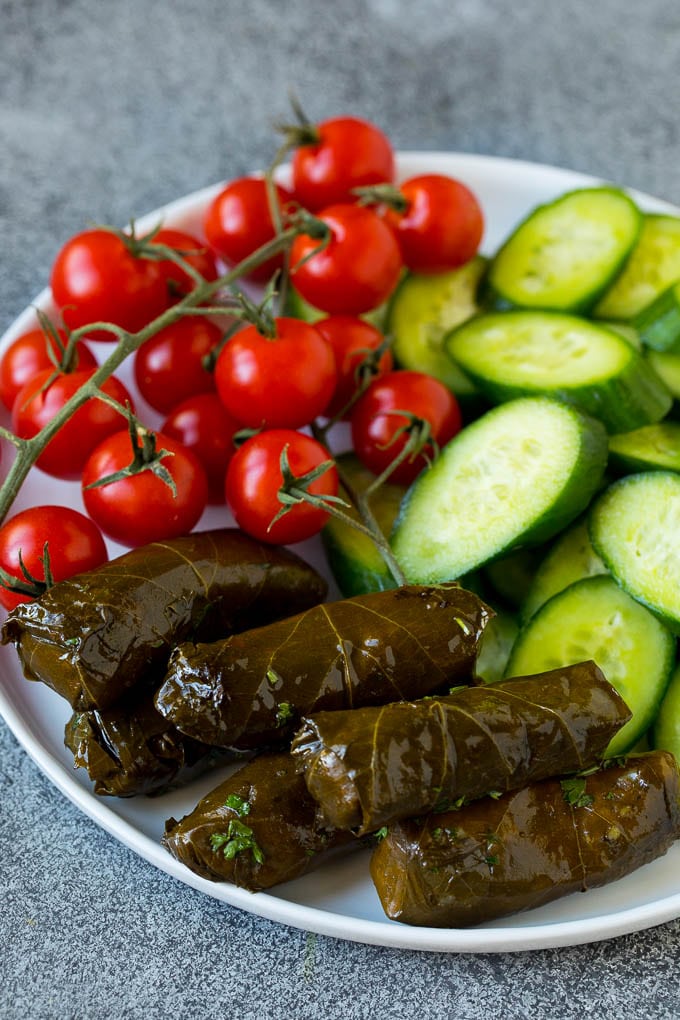 This mezze platter is filled with Mediterranean delicacies including dolmas, hummus, vegetables, pita bread and salads. #appetizer #ezlod A plate of cherry tomatoes, cucumber slices and dolmas.