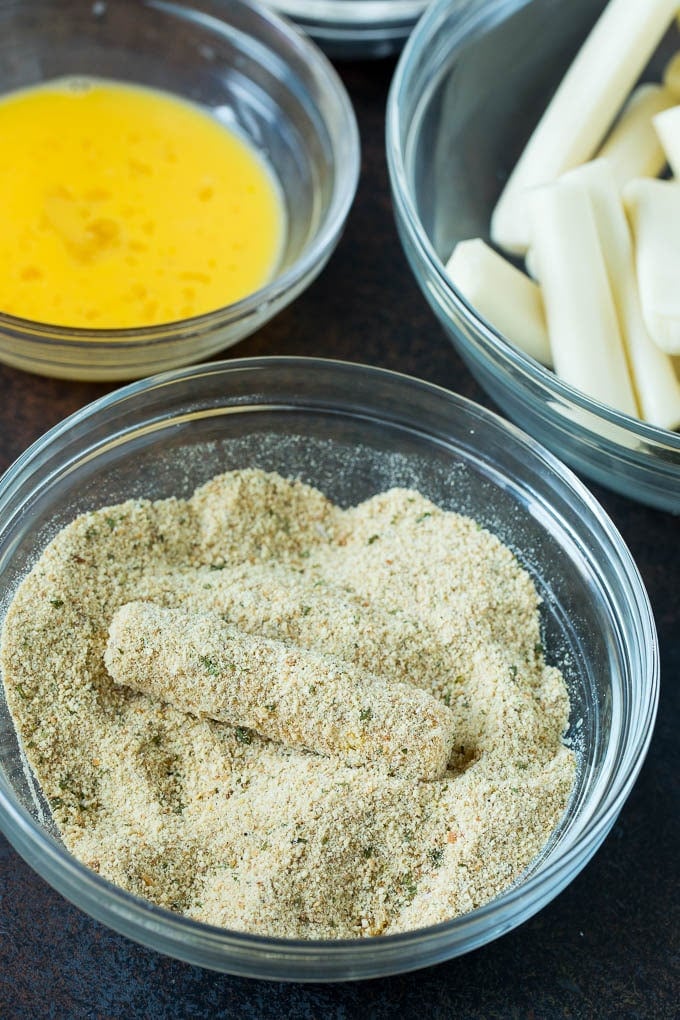 Mozzarella Sticks Recipe #cheese #appetizer #ezlod Cheese in a bowl of seasoned breadcrumbs.