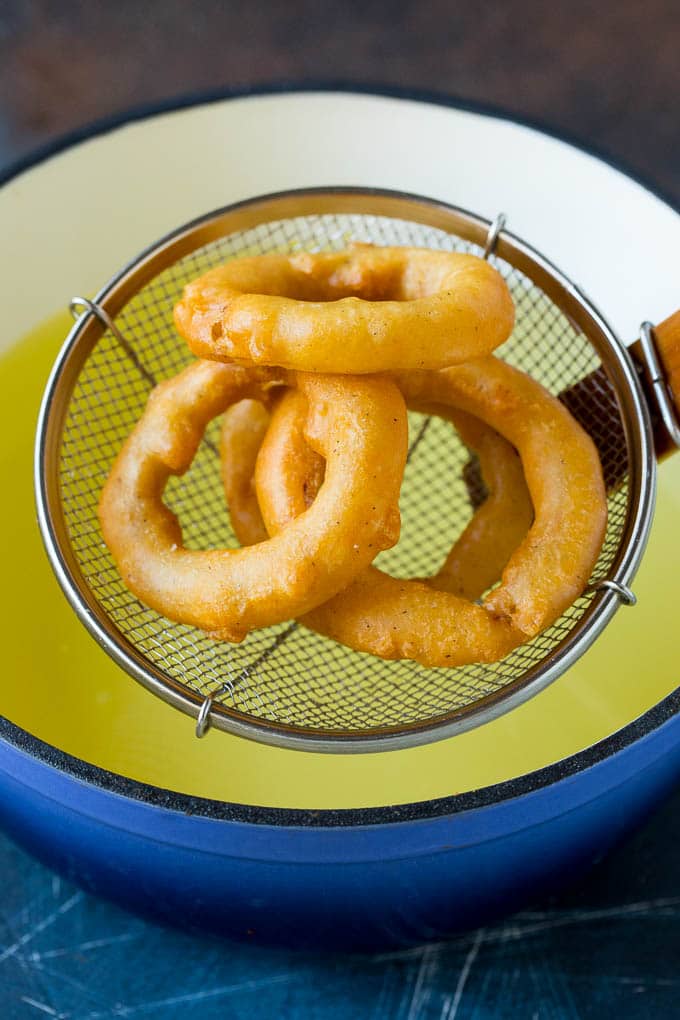 Crispy homemade onion rings that are fried in a flavorful beer batter. #onions #ezlod #appetizer Fried onions coming out of a pot of oil.