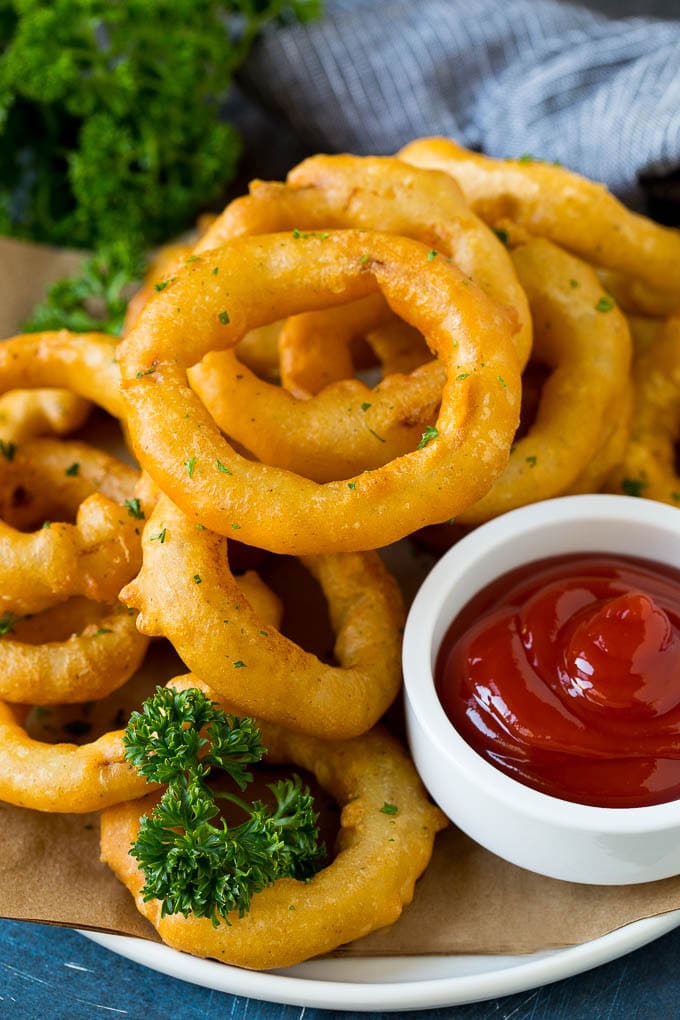Crispy homemade onion rings that are fried in a flavorful beer batter. #onions #ezlod #appetizer Fried onion rings on a plate with a side of ketchup.