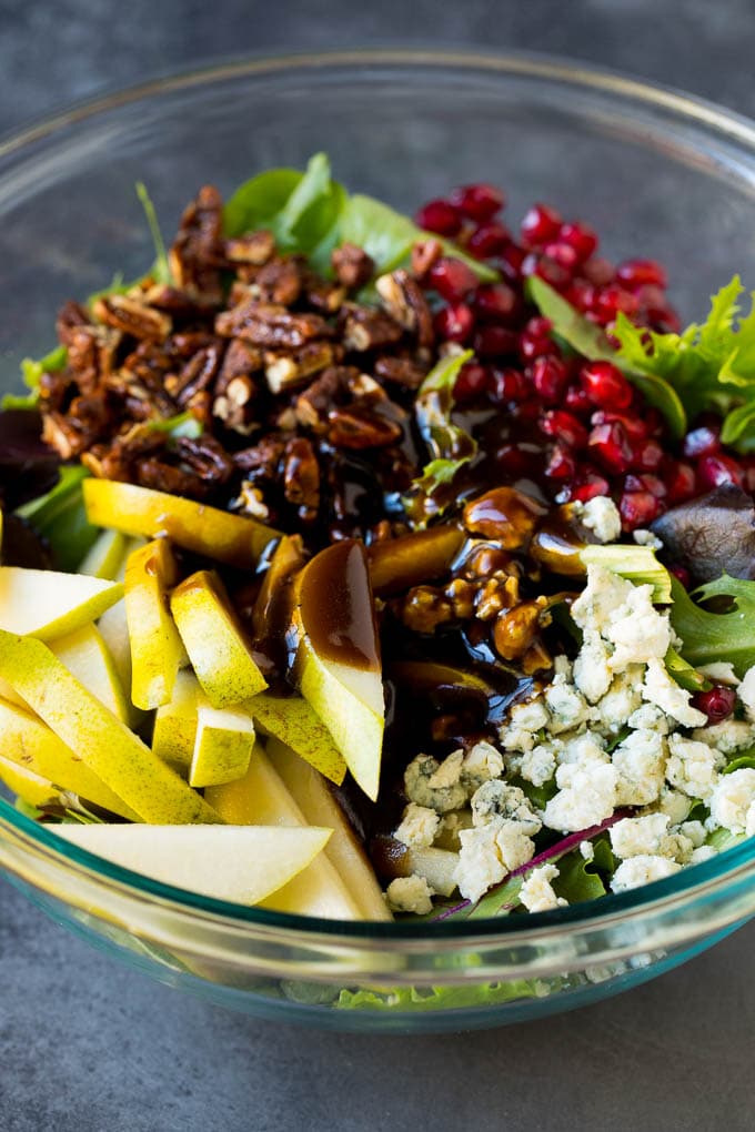 Pear Salad Recipe #salad #pears #fall #winter #dinner #ezlod Balsamic dressing poured over a bowl of mixed greens, fruit and pomegranate seeds.