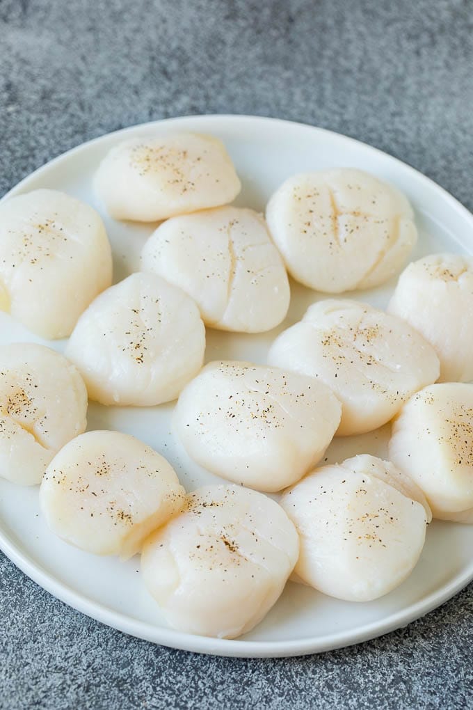Seared scallops with a garlic and herb butter sauce. An easy and elegant dinner! #seafood #dinner #ezlod Raw sea scallops on a plate.