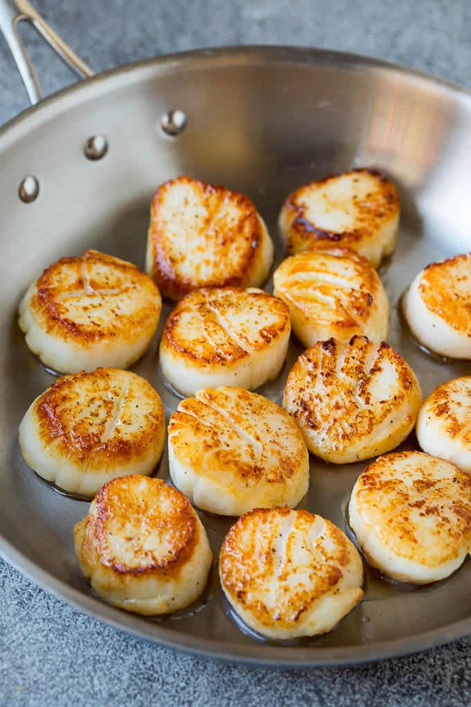 Seared scallops with a garlic and herb butter sauce. An easy and elegant dinner! #seafood #dinner #ezlod Scallops cooked to golden brown in a pan.