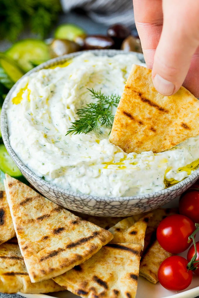 The best homemade tzatziki sauce with cucumber and herbs mixed into Greek yogurt. #appetizer #ezlod A hand dipping pita bread into a bowl of tzatziki.