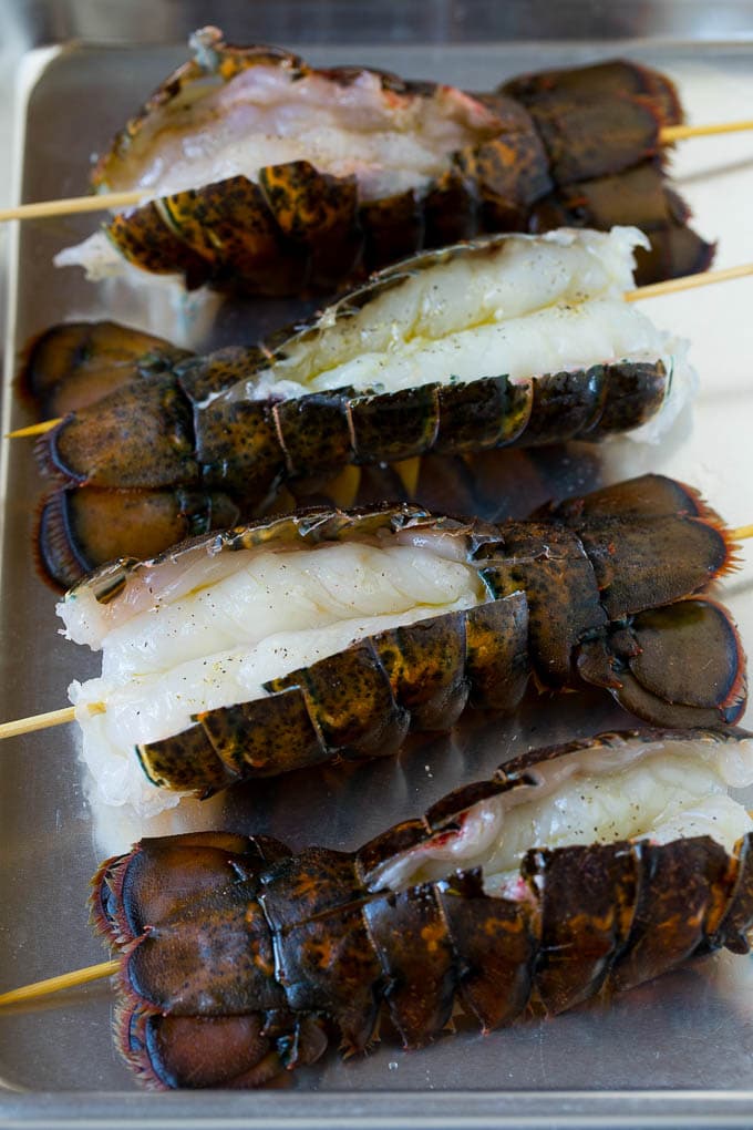 Grilled lobster tail drizzled with garlic butter is an easy and elegant dinner option. #lobster #ezlod Raw lobster tails split open with skewers through them.