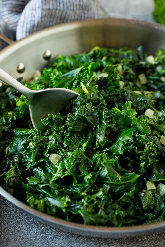 Sauteed kale flavored with olive oil and garlic, a quick and easy side dish! #kale #ezlod A pan of sauteed kale with a serving spoon in it.