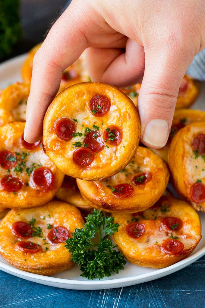 Mini pizzas topped with pepperoni are a fun and easy appetizer option. #pizza #ezlod #appetizer A platter of mini pizzas with a hand reaching for one.
