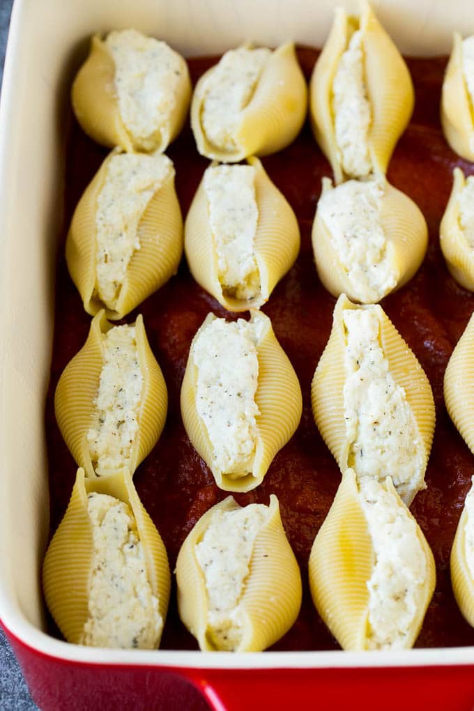 Baked stuffed shells filled with three types of cheese and topped with marinara sauce. #pasta #ezlod Pasta filled with cheese on a bed of tomato sauce.