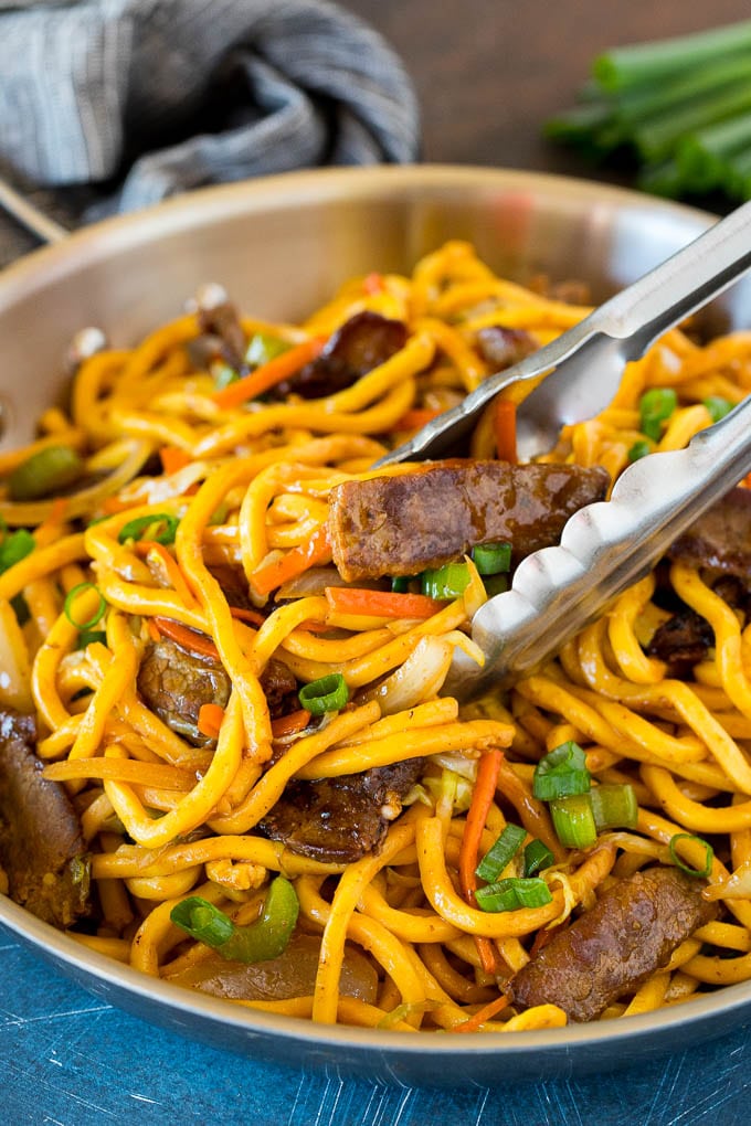 This beef lo mein is stir fried steak and vegetables tossed with egg noodles in a savory sauce. Tongs serving up a portion of beef lo mein.