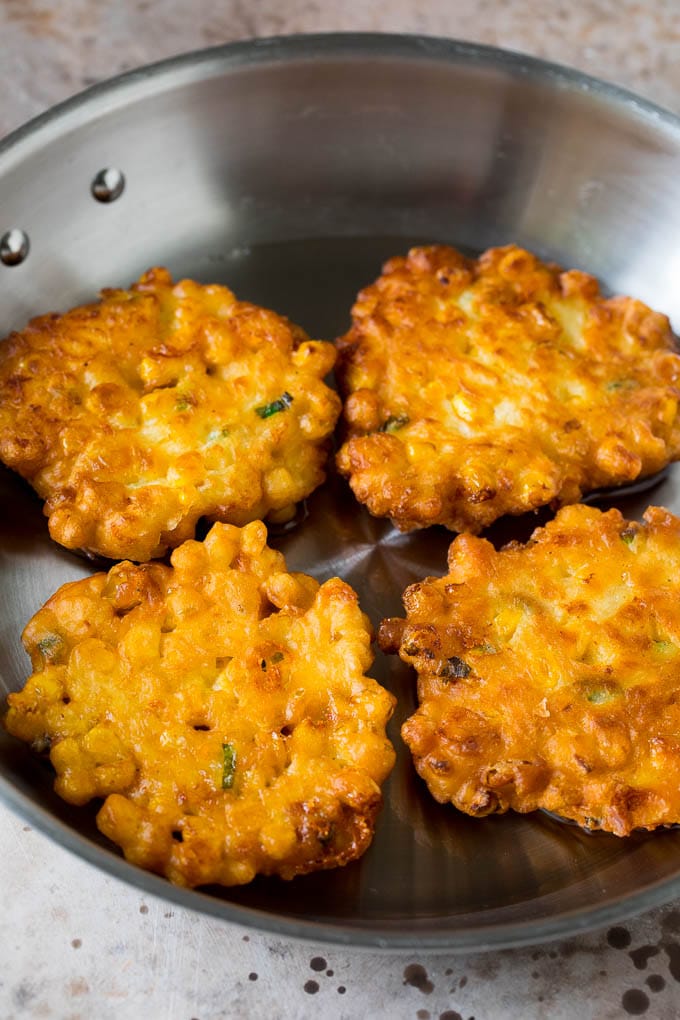 These crispy corn fritters are easy to make and are the perfect appetizer or lighter main course. #corn #ezlod Corn cakes in a pan of oil.
