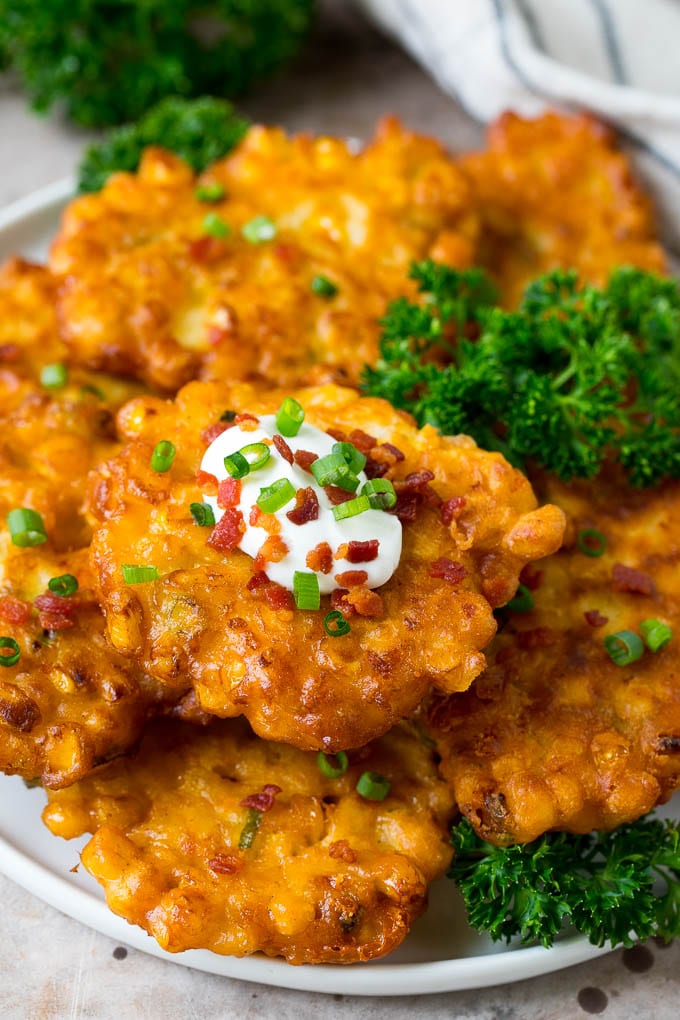 These crispy corn fritters are easy to make and are the perfect appetizer or lighter main course. #corn #ezlod A plate of corn fritters garnished with parsley, and topped with sour cream.