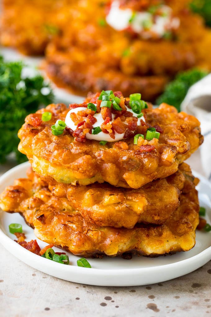These crispy corn fritters are easy to make and are the perfect appetizer or lighter main course. #corn #ezlod A stack of corn fritters topped with bacon, sour cream and green onions.
