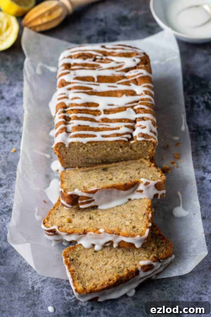 A beautifully baked vegan courgette cake loaf, drizzled with lemon glaze, rests on baking parchment next to fresh lemons and a bowl of glaze, creating an inviting rustic scene.