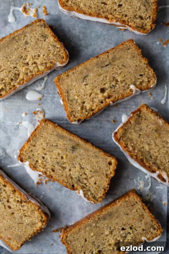 Several moist slices of freshly baked vegan courgette loaf cake are neatly arranged on a sheet of baking parchment, showcasing their inviting texture.
