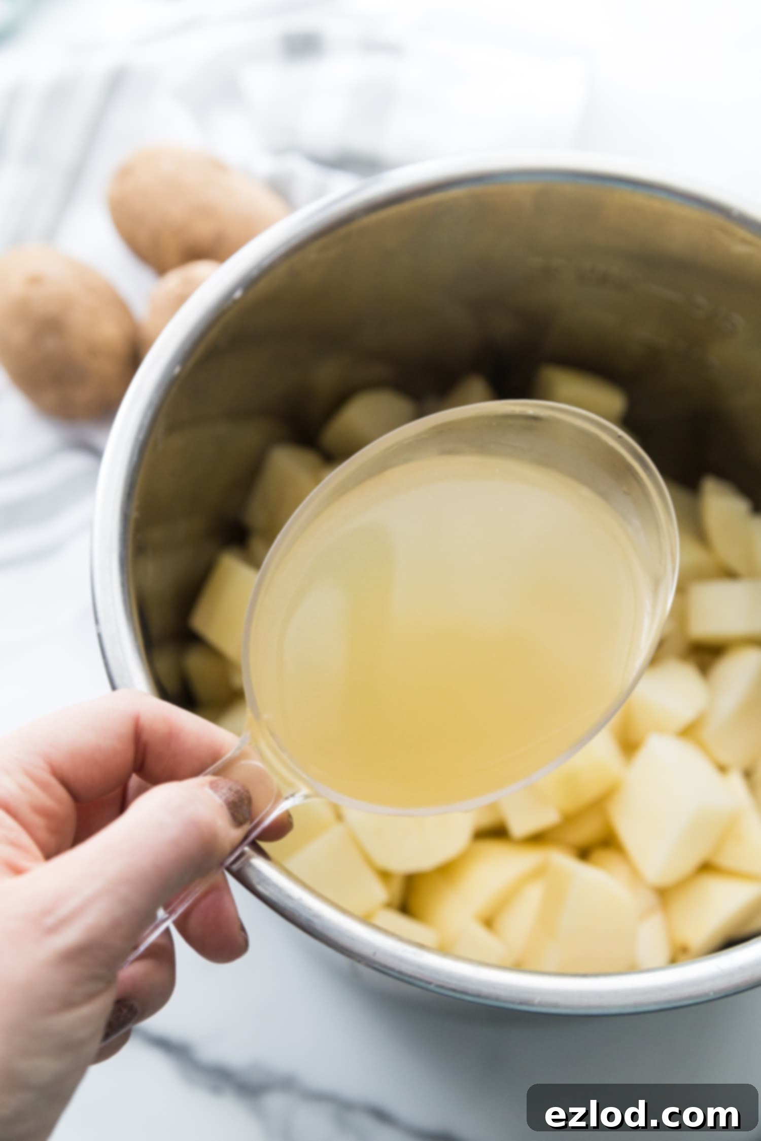 Photo of chicken broth in a measuring cup over a pot of diced potatoes for a dairy free instant pot mashed potatoes recipe.