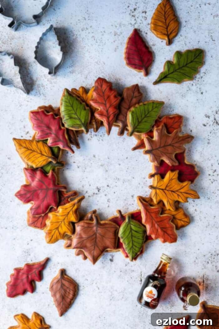 Autumn leaf maple cookie wreath on a white background with coloured leaf cookies, cookie cutters and bottles of maple syrup.