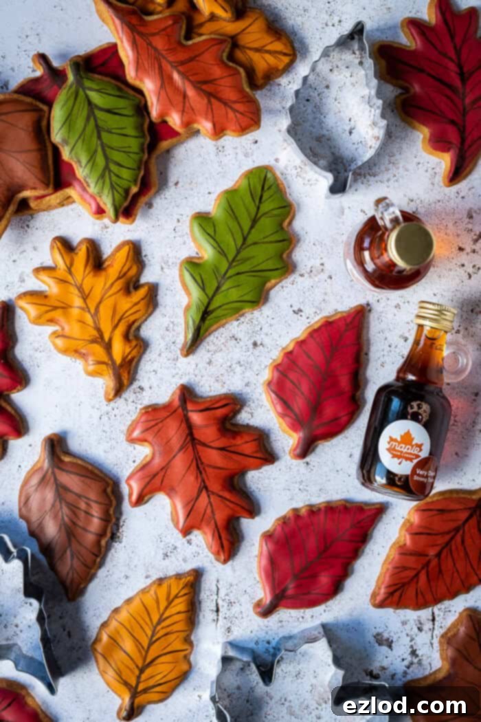 Coloured leaf biscuits on a white background with cookie cutters and bottles of maple syrup.