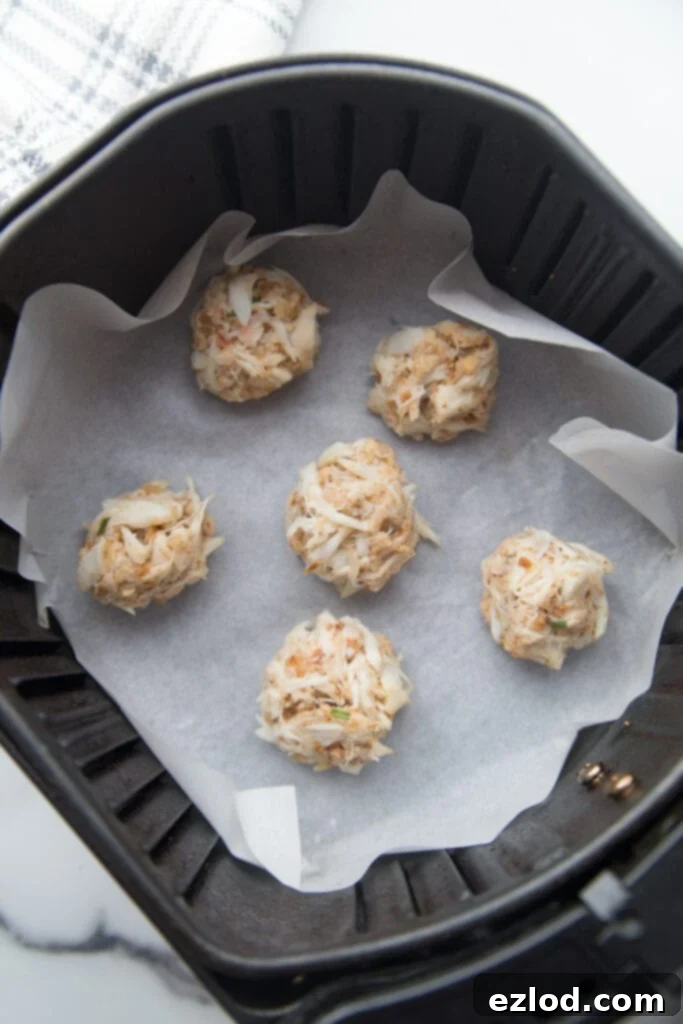 An air fryer basket lined with parchment paper with mini crab cakes