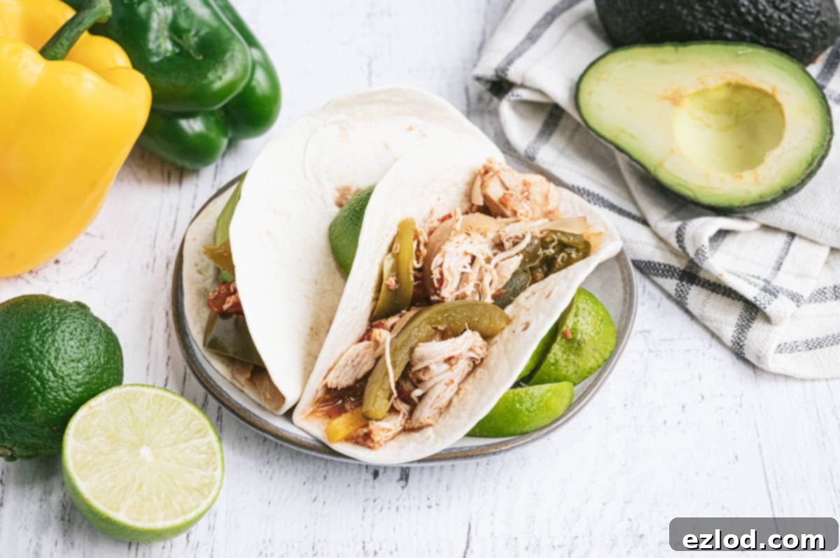 Effortless Slow Cooker Chicken Fajitas 3 Warm white corn tortillas filled with flavorful shredded Crockpot Chicken Fajitas and a slice of lime on a plate.