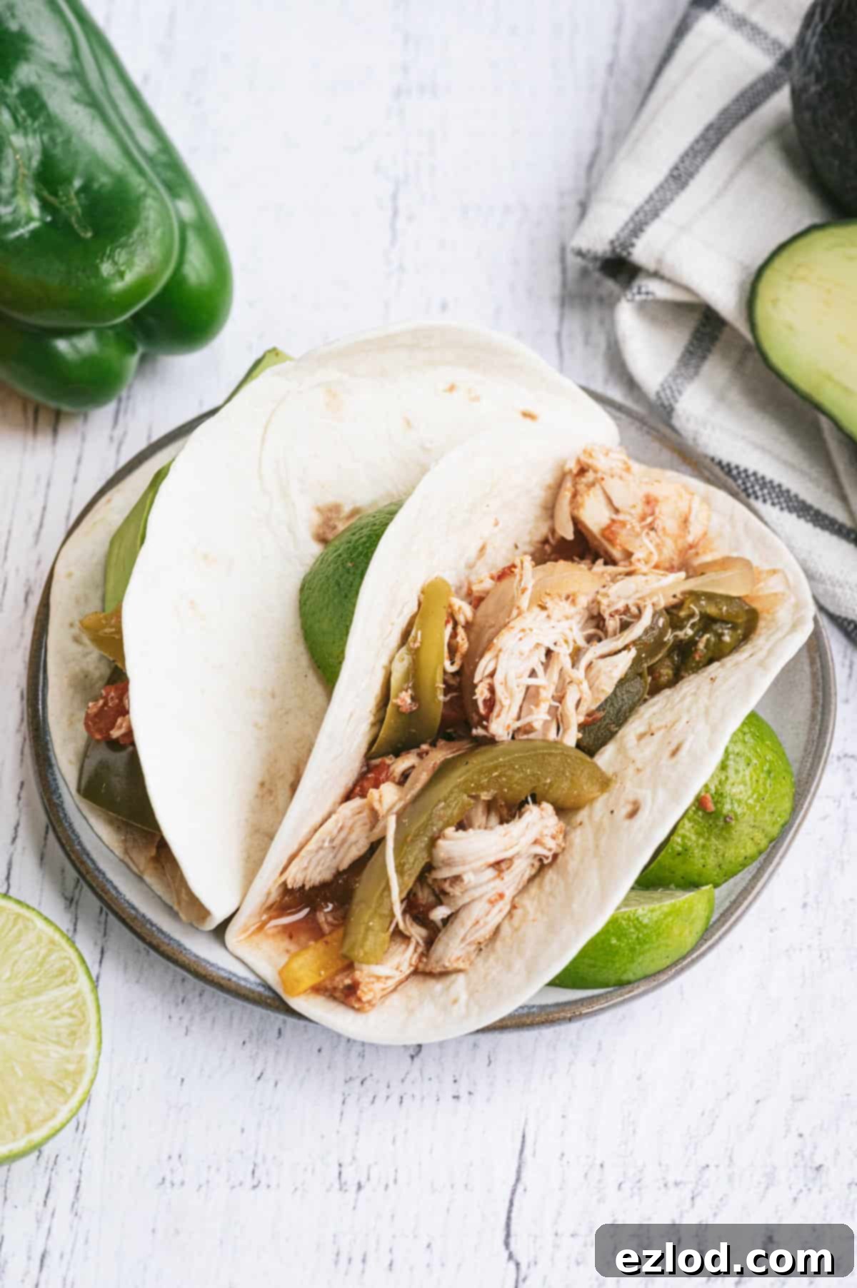 Effortless Slow Cooker Chicken Fajitas 5 Plated Crockpot Chicken Fajitas served in warm corn tortillas with a fresh lime wedge and fresh cilantro on a white wooden background.
