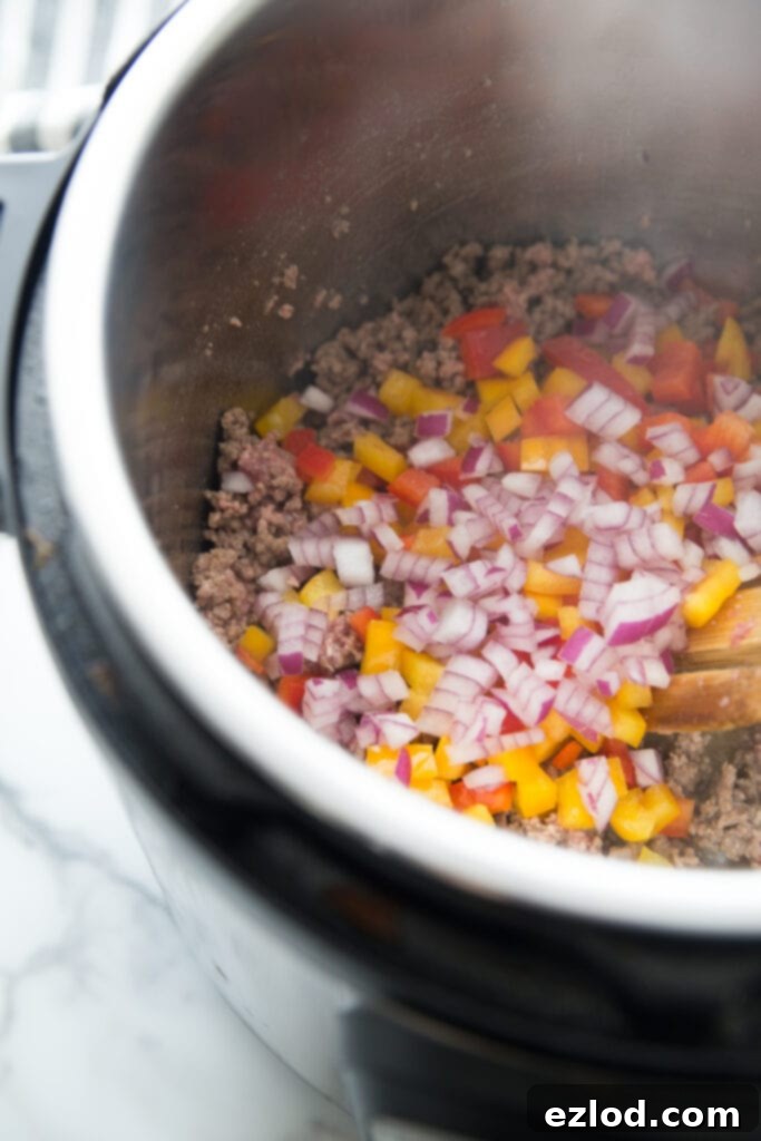Close-up shot showing ground beef browning with diced red onions and bell peppers in an Instant Pot, a key step in preparing the Instant Pot Beef Enchilada Pasta base, highlighting fresh ingredients and easy prep.