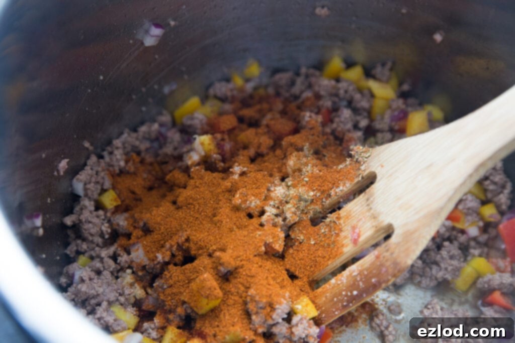 An aerial view inside an Instant Pot, showcasing a rich blend of homemade enchilada spices, diced red onion, and browned ground beef, ready to be stirred together before adding other ingredients for the Instant Pot Enchilada Pasta.