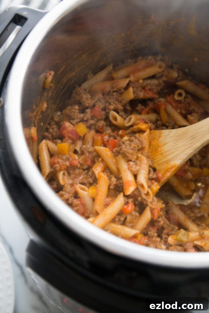 A wooden spoon stirring a generous portion of Instant Pot Enchilada Pasta, showcasing the melted cheddar cheese and vibrant mixture, ready to be served as a wholesome and delicious 21 Day Fix and WW friendly meal.