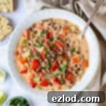 Easy Vegan Black-Eyed Pea Soup 2 A white bowlful of vegan black-eyed bean soup surrounded by a cream coloured cloth, bread, lime wedges and chopped herbs.